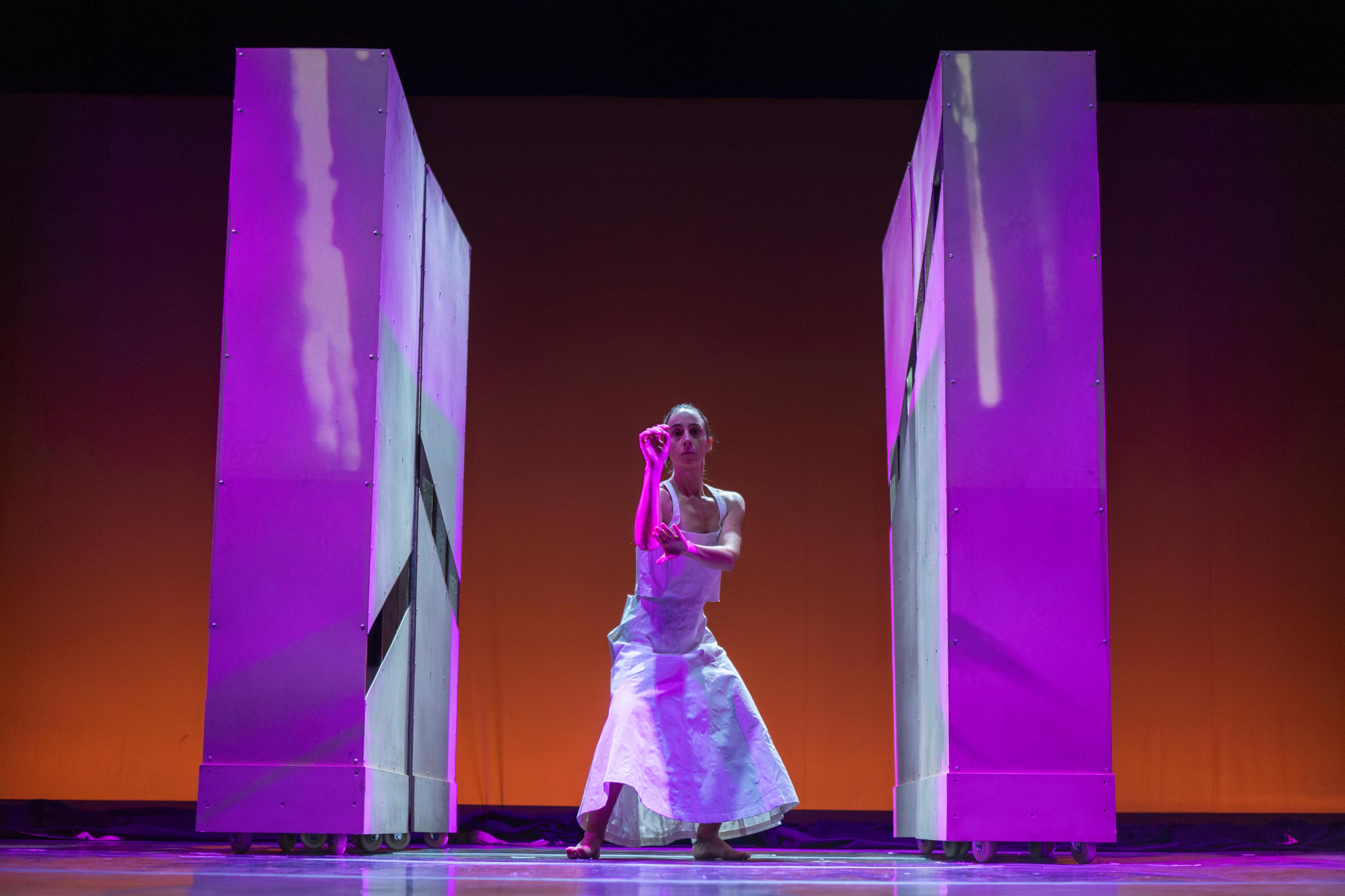 Dancer framed by tall stage panels under magenta light.