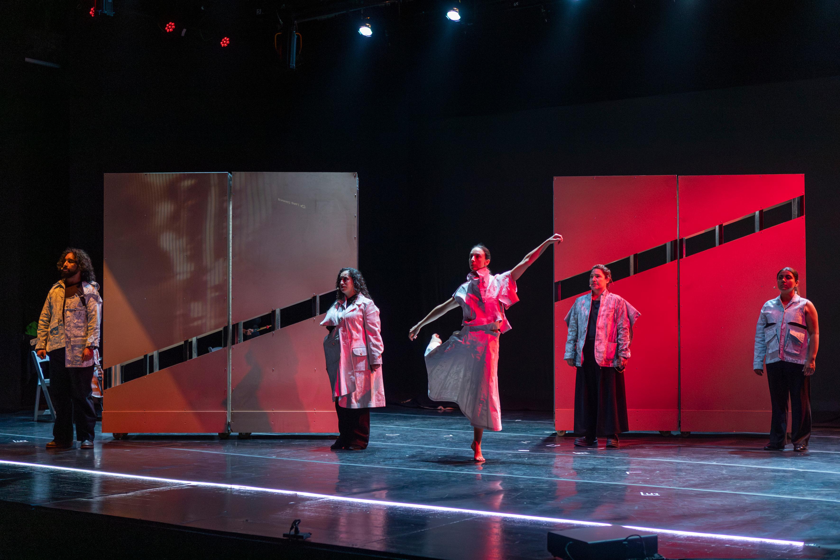 Performers on a stage with red sculptural panels.
